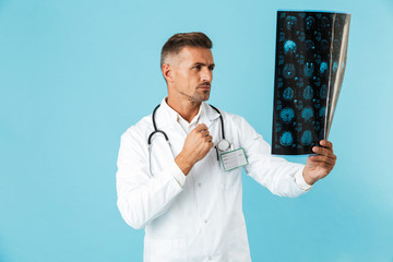 Portrait of professional medical doctor with stethoscope holding x-rays image, standing isolated...