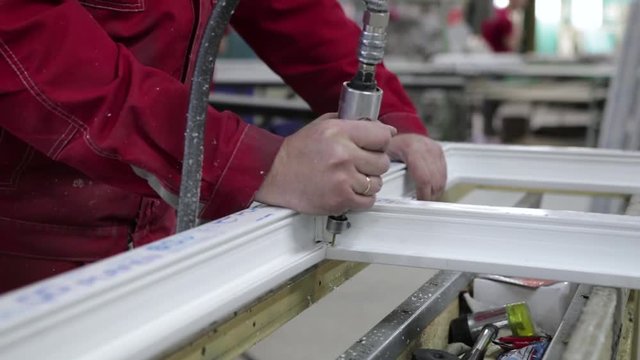 Manufacture of plastic windows and doors. Worker fastens the fittings with a screwdriver to the plastic window in the shop for the production of plastic and metal windows and doors. Screwing screws.