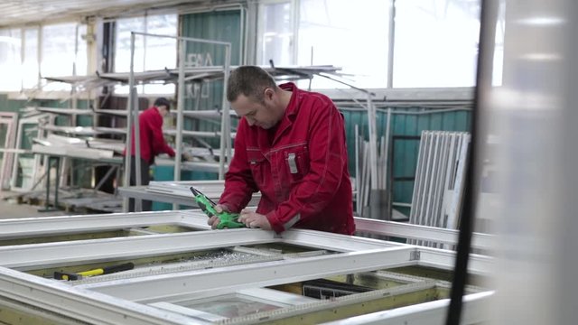 Manufacture of plastic windows and doors. Worker fastens the fittings with a screwdriver to the plastic window in the shop for the production of plastic and metal windows and doors. Screwing screws.