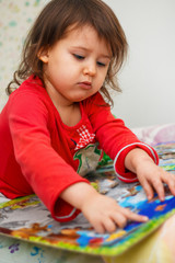 little girl Caucasian appearance in pajamas collects puzzles in a room