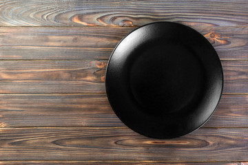 Directy above Empty black matte dish for dinner on wooden background with copy space