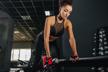 Attractive fitness woman in black sportswear top and leggins with perfect body posing in the gym. Sport workout exercises with dumbbels. Still dumbells.