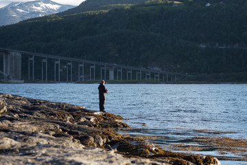 Fototapeta na wymiar Man fishing in fjord near the bridge. Norway
