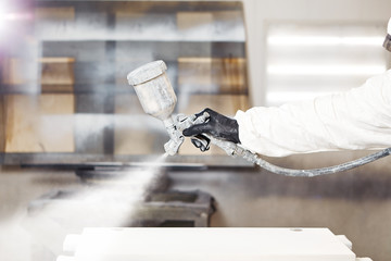 Close-up portrait of worker using spray gun and painting wood.