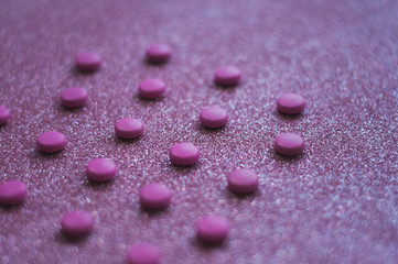 Pink pills, medicine isolated on glittery pink background.
