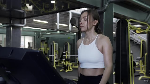 4K - Beautiful Young Woman Athlete Walks On A Treadmill Ending An Exercise Session In The Gym. Healthy Lifestyle Concept
