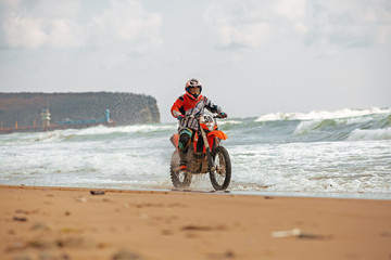 Obraz premium Motorcyclist in a protective suit rides a motorcycle on the sea, splashes fly from under the wheels.