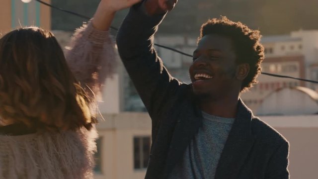 happy young multiracial couple dancing on rooftop at sunset celebrating relationship having fun enjoying playful dance together