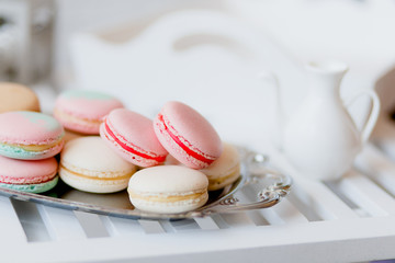 Colorful french macaroons (macarons) on steel tray with tea set on white wooden table