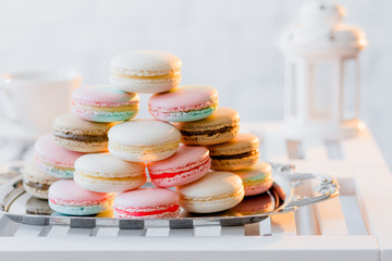 Colorful pastel pink, blue, yellow, beige and brown french macaroons on steel tray on white wooden table. Macarons close up.