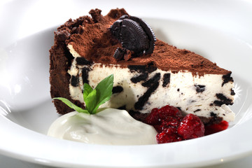 Kremowy tort  z czekoladą i ciasteczkami podany z bitą śmietana i sosem wiśniowym.