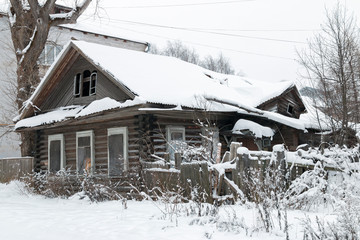 Old Russian abandoned collapsing wooden house with boarded up windows in winter under snow