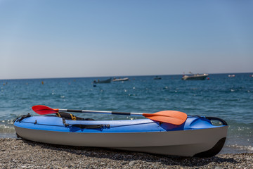 Blue and white kayak parked on the shore of a beautiful beach, on a sunny day
