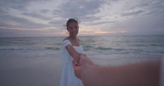 Young couple holding hands woman leading boyfriends walking towards beach sunset. POV travel holidays vacation concept. Shot on RED cinema Camera in SLOW MOTION.