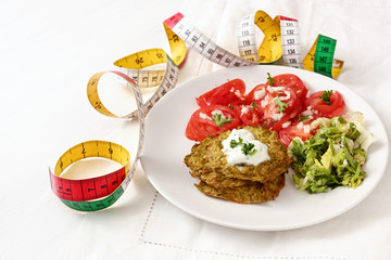 broccoli pancakes with yoghurt dip, lettuce and tomato, and a tape measure, healthy slimming food, white plate on a white tablecloth