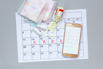women's calendar with marks on gray background. Tampons for menstruation, Sanitary pads, pills and smartphone. Hygiene care during critical days. Regular menstrual cycle. stomach pain. pms