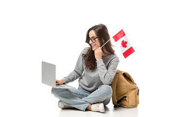 female student sitting with canadian flag and using laptop isolated on white