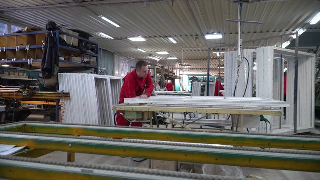 Manufacture of plastic windows and doors. Worker fastens the fittings with a screwdriver to the plastic window in the shop for the production of plastic and metal windows and doors. Screwing screws.