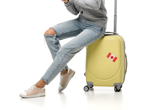cropped view of woman sitting on suitcase with canadian flag sticker isolated on white, travel concept