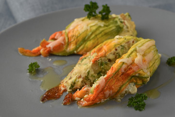 stuffed zucchini or courgette flowers baked with parmesan cheese and parsley garnish on a gray plate