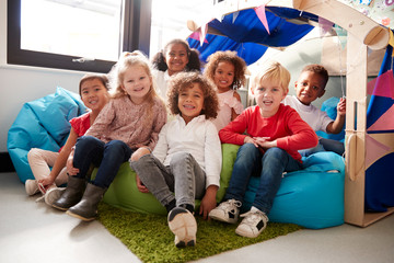 A multi-ethnic group of infant school children sitting on bean bags in a comfortable corner of the classroom, smiling to camera, low angle, close up