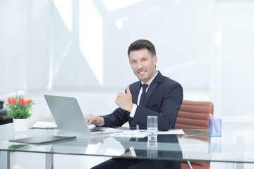 close up.smiling businessman working on laptop and showing thumb up