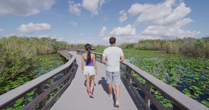 Everglades National Park Trail - tourists visiting Florida Everglades. Couple on travel in Miami doing day tour to Everglades walking Anhinga Trail. RED EPIC SLOW MOTION.