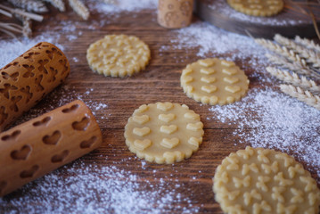 Cutting cookies with a print of butterflies and hearts on the wooden table. Wooden rolling pins in the picture
