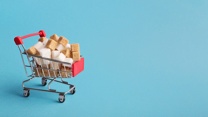 Shopping cart with sugar cubes on blue background