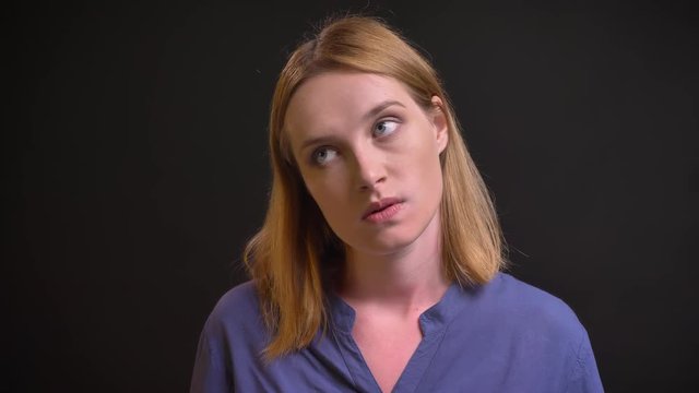Portrait of formally-dressed tired woman watching into camera with passivity on black background.