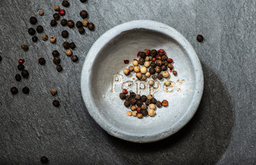 Black pepper in small bowl for spices on dark background. Bowl with text Pepper on the bottom.