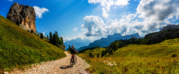 Tourist cycling in Cortina d'Ampezzo, stunning rocky mountains on the background. Woman riding MTB enduro flow trail. South Tyrol province of Italy, Dolomites.