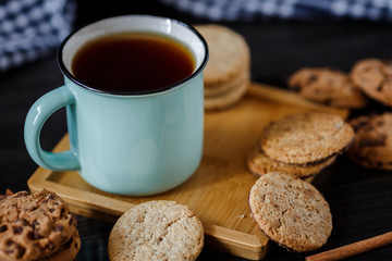 Cup of tea and various cookies on dark wooden background