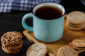 Cup of tea and various cookies on dark wooden background