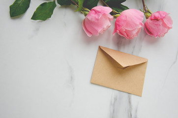 Pink roses and a craft envelope on marble table.Concept of greeting