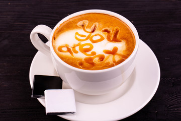 A cappuccino cup with two chocolates and an inscription from caramel