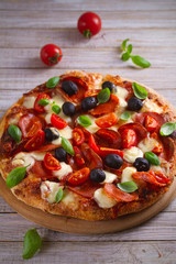  Pizza with pepperoni, tomatoes, cheese, olives and basil. Delicious pizza served on wooden plate on rustic background. vertical