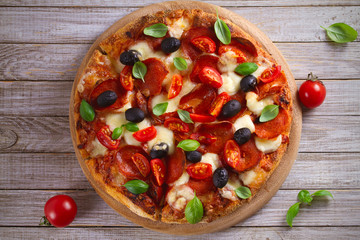  Pizza with pepperoni, tomatoes, cheese, olives and basil. Delicious pizza served on wooden plate on rustic background. overhead, horizontal