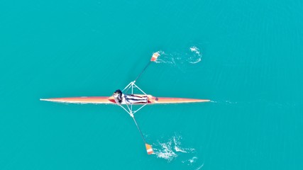 Aerial drone bird's eye view of sport canoe operated by young fit man in turquoise clear waters