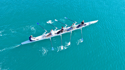 Aerial drone bird's eye view of sport canoe operated by team of young women in emerald clear sea
