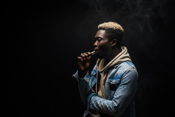 African Man smoking or vaping e-cig or electronic cigarette holding a mod with a lot of clouds isolated on black background