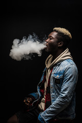 African Man smoking or vaping e-cig or electronic cigarette holding a mod with a lot of clouds isolated on black background