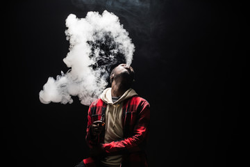 Young african man on a black background holding an electronic cigarette, vaping device, mod, e-cig...