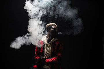Young african man holding and vaping an electronic cigarette, e-cig, ecigarette isolated on black background.
