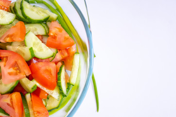 Fresh vegetable salad of tomatoes and cucumbers in a transparent glass plate, which stands on a white background.