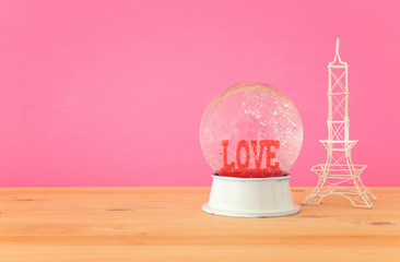 Valentine's day background. Water globe with word LOVE and glitter next eiffel tower, over the...