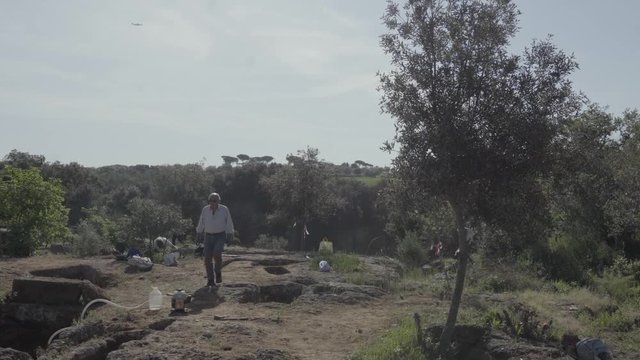 People walking around Etruscan burial plots scattered around landscape.