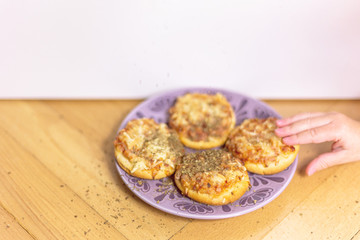 Four mini pizzas and a child's hand