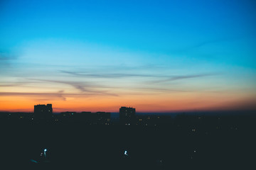 Fototapeta premium Cityscape with wonderful varicolored vivid dawn. Amazing dramatic blue sky with purple and violet clouds above dark silhouettes of city buildings. Atmospheric background of orange sunrise. Copy space.