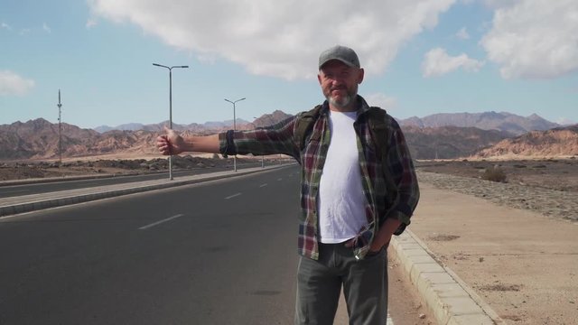 Senior male stand on a road and showing thumb up in hitchhiking sign